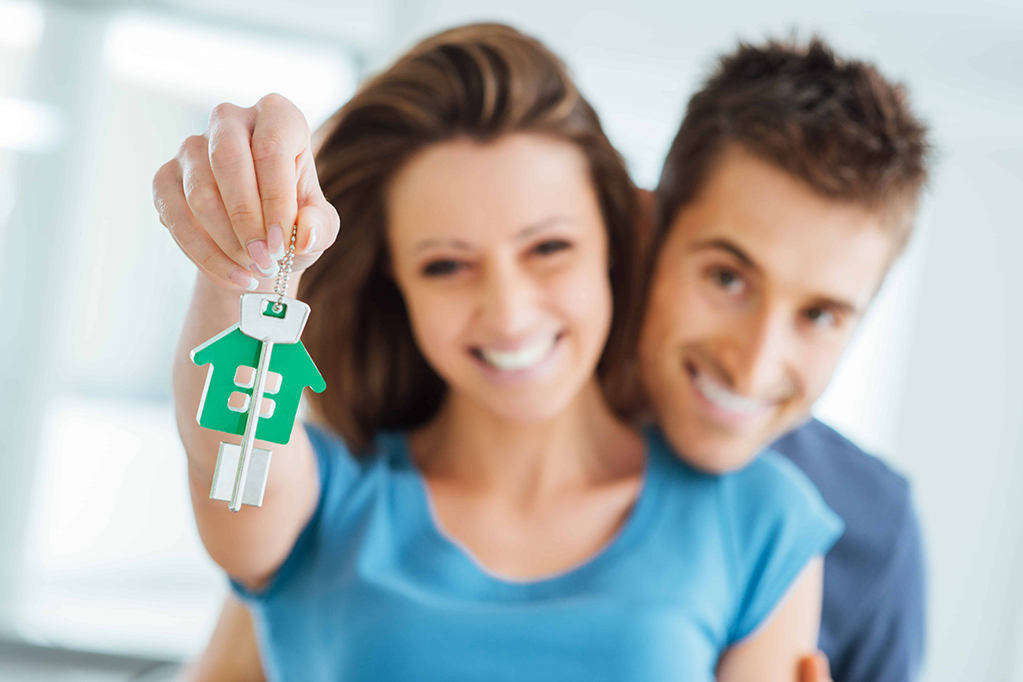  Young smiling couple holding their new house keys, real estate and relocation concept 