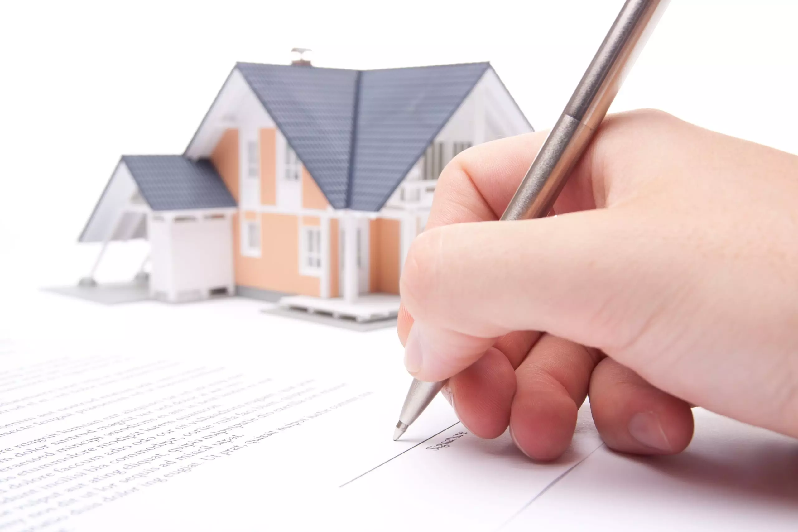 Hand signing document in front of model house